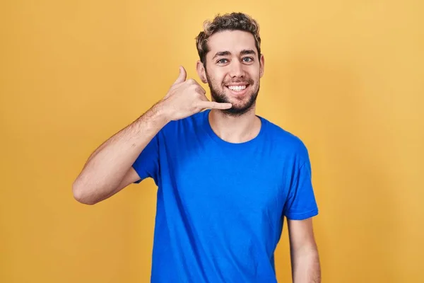 髭を生やしたヒスパニック系の男性が黄色い背景の上に立ち 電話で話すような手や指で電話のジェスチャーをして笑っています コミュニケーションの概念 — ストック写真