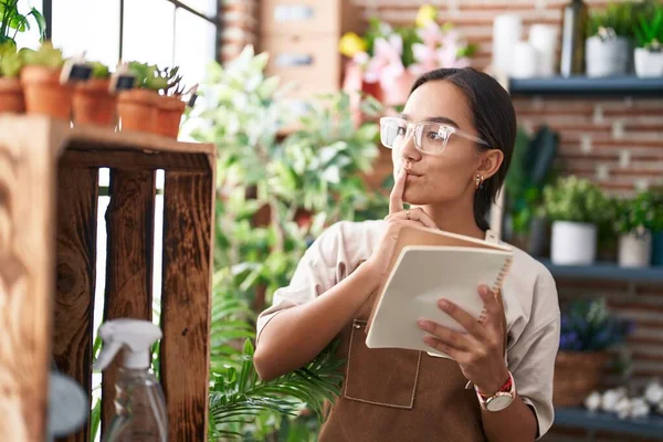 Çiçekçide kuşkulu bir ifadeyle not defteri okuyan güzel İspanyol kadın.
