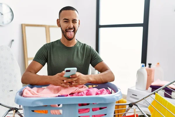 African American Man Doing Laundry Using Smartphone Sticking Tongue Out — Stockfoto
