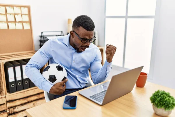 Young african man football hooligan cheering game at the office annoyed and frustrated shouting with anger, yelling crazy with anger and hand raised