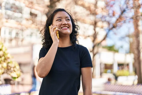 若いです中国人女性笑顔自信を持って話して上のスマートフォンで公園 — ストック写真
