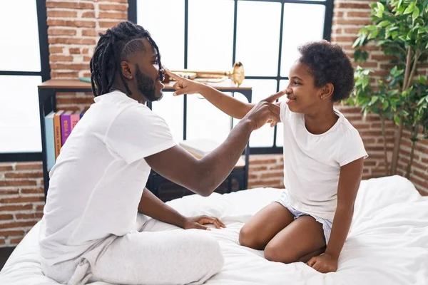 Father and daughter touching nose with finger sitting on bed at bedroom