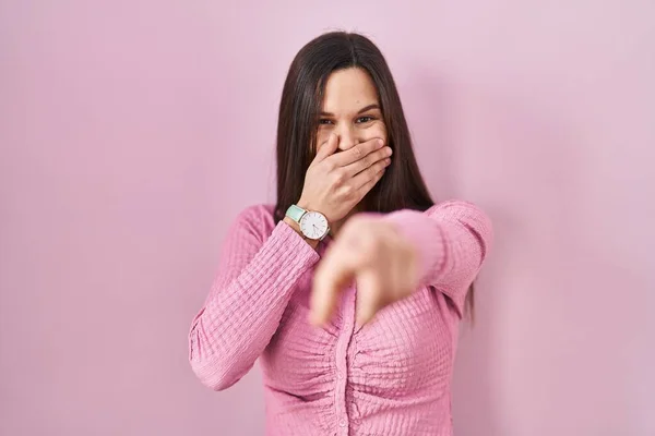 若いヒスパニック系の女性がピンクの背景に立ってあなたを笑って 手で口の上にカメラに指を指して 恥の表情 — ストック写真