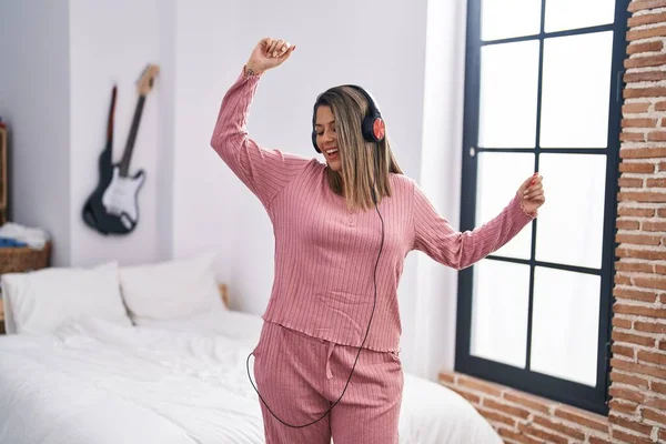 Young hispanic woman listening to music and dancing at bedroom