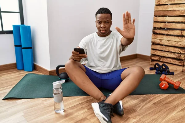 Hombre Africano Joven Sentado Alfombra Entrenamiento Gimnasio Usando Teléfono Inteligente —  Fotos de Stock