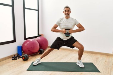 Spor merkezinde kettlebell eğitimi alan orta yaşlı gri saçlı bir adam.