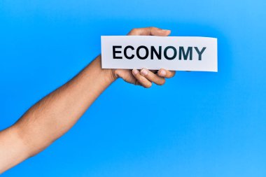 Hand of caucasian man holding paper with economy word over isolated blue background