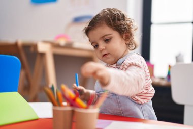 Anaokulunda masaya oturmuş kağıda resim çizen sevimli İspanyol kız öğrenci.