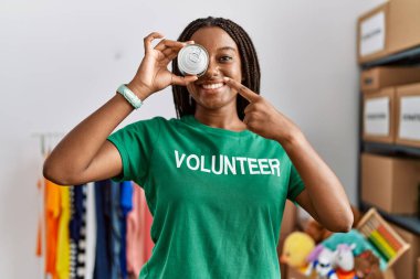 Gönüllü üniformalı genç Afro-Amerikan kadın yardım merkezinde konserve yiyecekleri tutuyor.