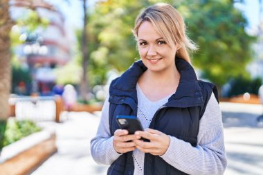 Parkta akıllı telefon kullanan, kendine güvenen genç sarışın kadın.