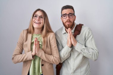 Young couple standing over white background begging and praying with hands together with hope expression on face very emotional and worried. begging. 