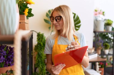 Young blonde woman florist smiling confident writing on document at flower shop