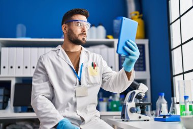 Laboratuvarda dokunmatik ped kullanan genç bir İspanyol bilim adamı üniforması giyiyor.