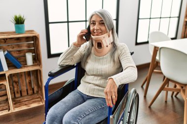 Orta yaşlı, kır saçlı, akıllı telefondan konuşan, tekerlekli sandalyede oturan bir kadın.