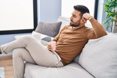 Genç İspanyol adam evdeki kanepede kahve içiyor.