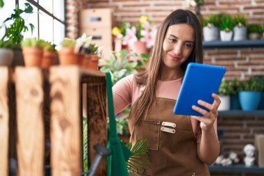 Young beautiful hispanic woman florist smiling confident using touchpad at flower shop