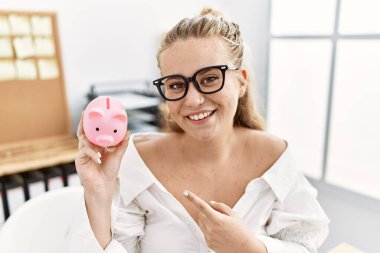 Kumbarayı tutan beyaz bir kadın gülümsüyor mutlu bir şekilde elini ve parmağını gösteriyor. 