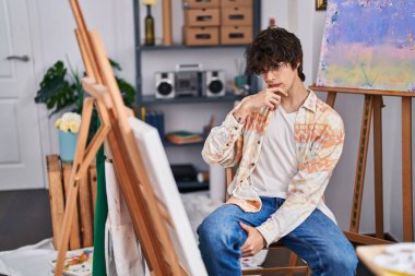Young hispanic man artist looking draw with doubt expression at art studio