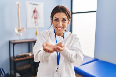 Young brunette woman working at pain recovery clinic smiling with hands palms together receiving or giving gesture. hold and protection 