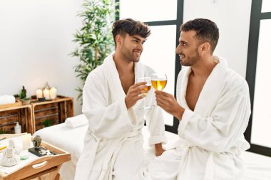 Şampanyayla kadeh kaldıran iki İspanyol erkek güzellik merkezinde masaj masasında oturuyor.