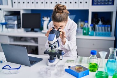 Adorable girl scientist using microscope working at laboratory