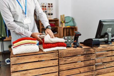 Orta yaşlı, gri saçlı, mağazada kıyafet katlayan bir tezgahtar.