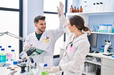 Man and woman wearing scientist uniform high five with hands raised up at laboratory