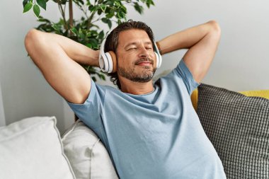 Middle age caucasian man relaxed with hands on head listening to music at home