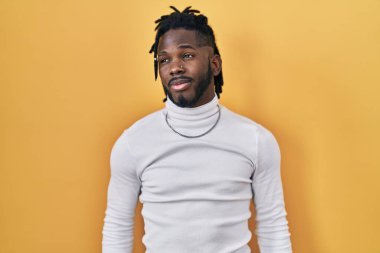 Sarı arka planda balıkçı yaka kazak giyen Afrikalı adam gülümsüyor ve başka tarafa bakıyor.. 