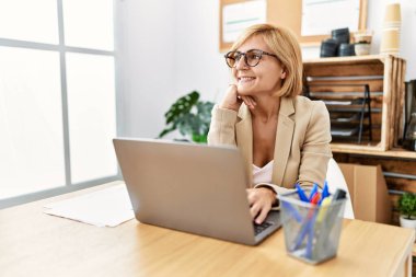 Ofiste çalışırken gülümseyen orta yaşlı sarışın kadın.