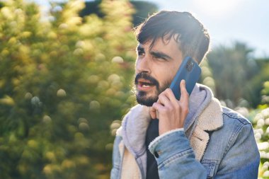 Genç İspanyol adam parkta akıllı telefondan konuşuyor.