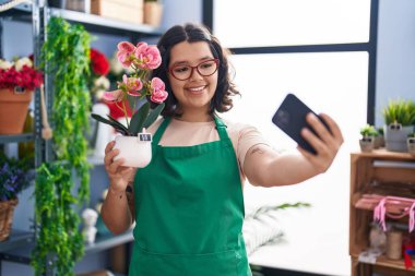 Young woman florist holding plant pot make selfie by smartphone at florist