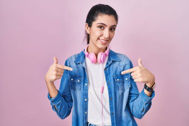 Young beautiful woman standing over pink background looking confident with smile on face, pointing oneself with fingers proud and happy. 