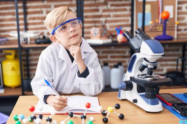 Sınıfta şüpheli bir ifadeyle not defterine yazan sevimli çocuk.