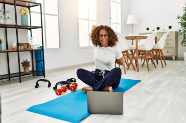 Middle age hispanic woman stretching using laptop at home