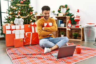 Genç Arap adam evdeki Noel ağacının yanında dizüstü bilgisayar kullanıyor..