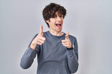 Young man standing over isolated background pointing fingers to camera with happy and funny face. good energy and vibes. 