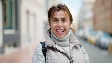 Orta yaşlı İspanyol kadın sokakta kendine güvenerek gülümsüyor.