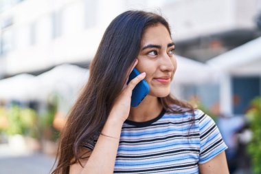 Young hispanic girl smiling confident talking on the smartphone at street