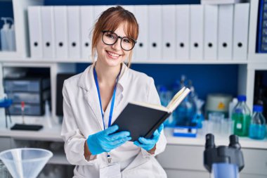 Genç bilim kadını gülümsemesi laboratuarda kendinden emin bir şekilde kitap okuyor.