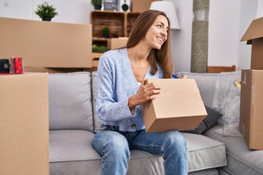 Young woman writing on package sitting on sofa at new home