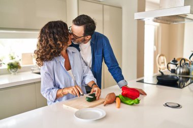 Middle age hispanic couple kissing and hugging each other cooking at kitchen