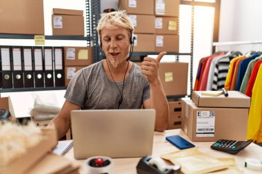 Young blond man wearing operator headset working at online shop smiling happy and positive, thumb up doing excellent and approval sign 