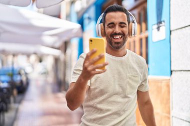 Genç İspanyol adam kendinden emin bir şekilde gülümsüyor müzik dinliyor ve sokakta dans ediyor