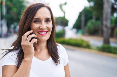 Genç, güzel, İspanyol bir kadın gülümsüyor ve caddede akıllı telefondan konuşuyor.