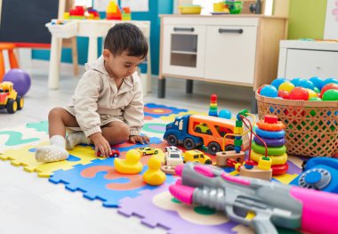 Adorable hispanic toddler playing with car toy sitting on floor at kindergarten