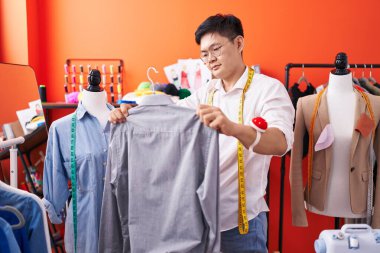 Young chinese man tailor holding shirt at atelier