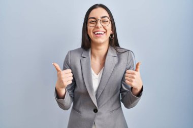 İspanyol iş kadını gözlük takıyor başarı işareti takıyor. Elleriyle olumlu jest yapıyor. Gülümsüyor ve mutlu. Neşeli ifade ve kazanan jest. 