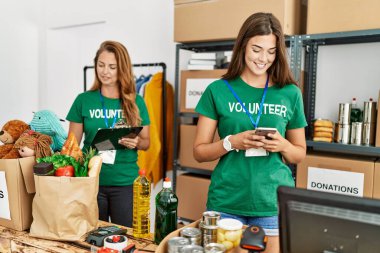 Anne ve kızı gönüllü üniforması giyip listeye yazıyorlar ve yardım merkezinde akıllı telefon kullanıyorlar.