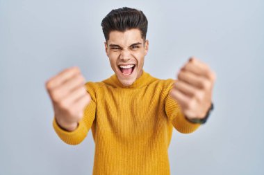 Mavi arka planda öfkeli ve kızgın duran genç İspanyol adam öfkeyle bağırırken kızgın ve öfkeli yumruklar sallıyor. öfke ve agresif konsept. 